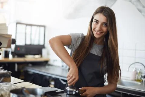 Young barista at work looking at camera smiling, using a tamper to prepare an Stock Photos