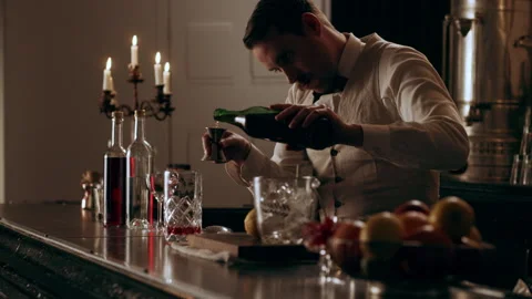 Young bartender with classic style, pouring shots of red liquor and putting cube Stock Footage 199463817