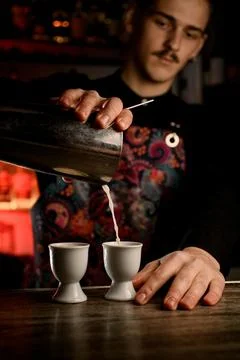Young bartender in dark clothes make a cocktails with a metal shaker 스톡 사진