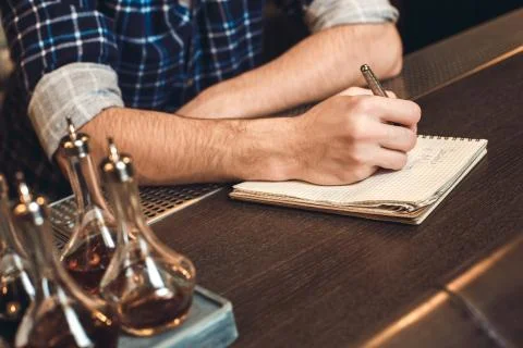Young bartender leaning on bar counter writing inventory close-up Stock Photos