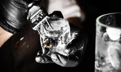 Young bartender with special device breaks pieces of ice. Many shards of ice Foto stock