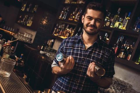 Young bartender standing at bar counter holding shaker playful Stock Photos