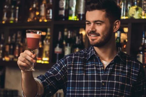 Young bartender standing at bar counter looking at cocktail smiling satisfied Stock Photos