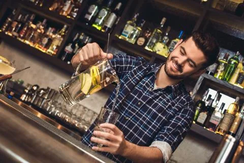Young bartender standing at bar counter pouring vitamin water into glass happy Stock Photos