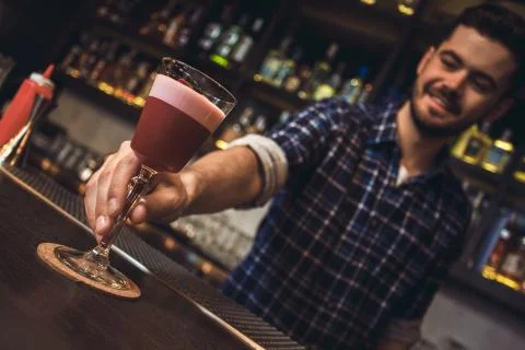Young bartender standing at bar counter serving cocktail close-up cheerful Stock Photos