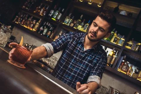 Young bartender standing at bar counter serving cocktail Stock Photos