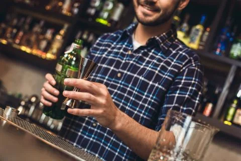 Young bartender standing at bar counter holding jigger with alcohol cheerful Stock Photos