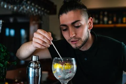 Young bartender stirring a mixed drink in a crystal glass with a slice of citrus Stock Photos