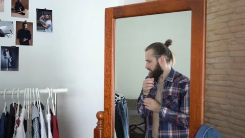 Young beard guy is looking into the mirror buttoning the shirt's sleeves Stock Footage 147893479