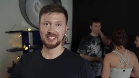 Young beard guy waving to the camera while people are chatting at the background Stock Footage 156476964