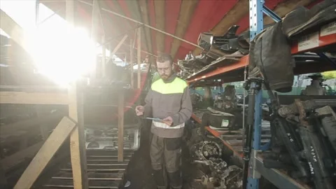 A young bearded auto mechanic with glasses walks between the shelves with a Stock Footage 136815744