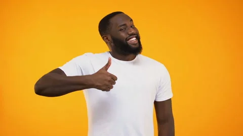 Young bearded black guy giving thumbs up, smiling at camera on yellow background 스톡 동영상 103292450