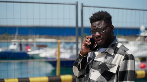 Young bearded black man is calling by phone and walking in city harbour, african Video stock 231901734