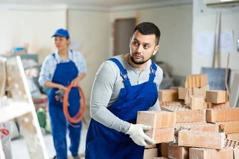 Young bearded builder stacking red bricks on construction site indoors Stock Photos