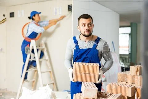 Young bearded builder stacking red bricks on construction site indoors Stock-Fotos