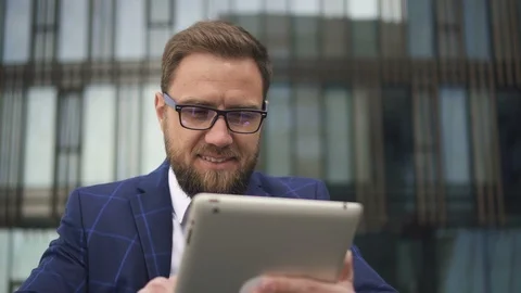 Young bearded business owner is using tablet, smiling on office building Video stock 91493996