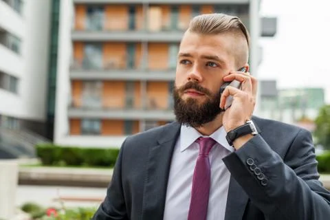 Young bearded businessman using mobile phone outside the office. Outdoor phot Stock Photos