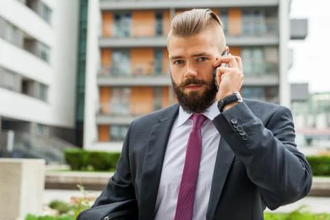 Young bearded businessman using mobile phone outside the office. Outdoor phot Stock-Fotos