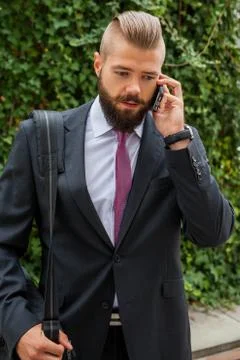 Young bearded businessman using mobile phone outside the office. Outdoor phot Stock Photos