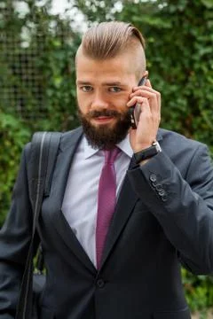 Young bearded businessman using mobile phone outside the office. Outdoor phot Stock Photos