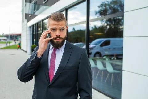 Young bearded businessman using mobile phone outside the office. Outdoor phot Stock Photos