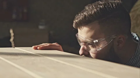 A young bearded carpenter checks the quality of the boards in the sun. RAW video Video stock 60704525