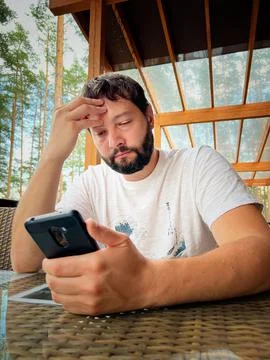 Young bearded caucasian man using smartphone sitting on terrace 写真素材