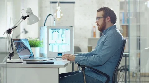 Young Bearded Developer Uses 3D Printer for Modeling. He is Sitting at His Desk  Stock Footage 70630480