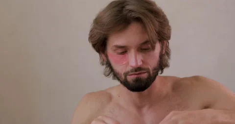 Young bearded guy applying korean eye patches and looking at camera. Isolated Stock Footage 142529506