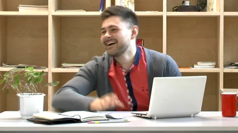 Young bearded guy  at his white laptop working, then laughs Stock Footage 62066793