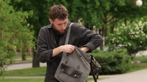 A young bearded guy is looking for something in his backpack Stock Footage 279741492