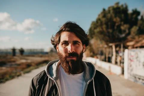 Young bearded guy portrait, looking at camera with the sun in a face side, wi Stock Photos
