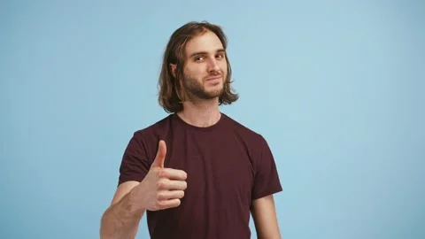Young bearded guy is shaking his head, showing thumbs up, winking and smiling Stock Footage 145075810