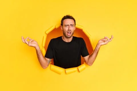 A young bearded guy stands in the middle of a hole in a yellow background, wears Stock-Fotos
