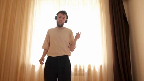 A young bearded guy wearing wireless headphones listens to music and dances to Stock Footage 278364193