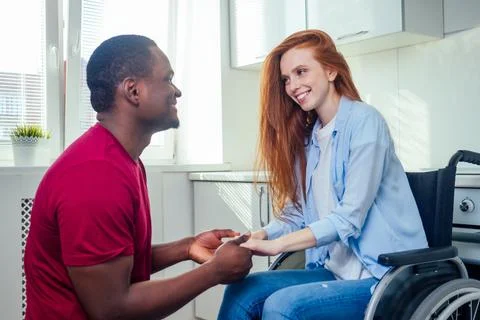 Young bearded handicapped redhaired ginger wife in wheelchair and her african Foto stock
