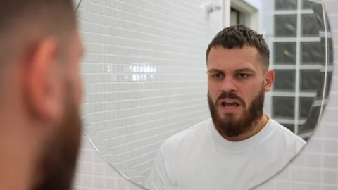 Young bearded handsome man talking to his reflection in bathroom mirror Stock-Footage 253012332
