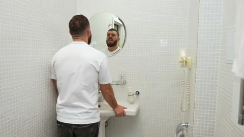 Young bearded handsome man talking to his reflection in bathroom mirror Stock Footage 255041846