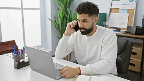 A young, bearded hispanic man in a white sweater is making a phone call whi.. Video stock 272995560