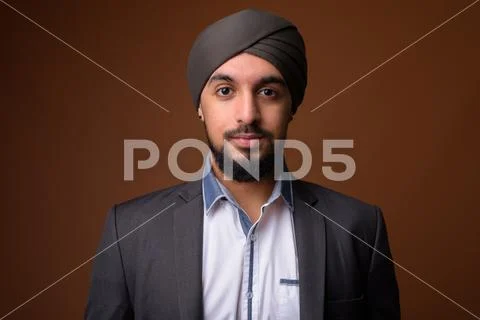 Young bearded Indian Sikh businessman wearing turban against bro Stock Photos