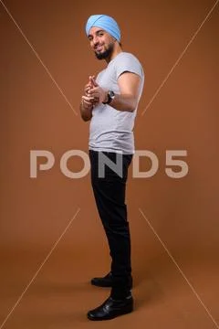 Young bearded Indian Sikh man wearing turban against brown backg Stock Photos