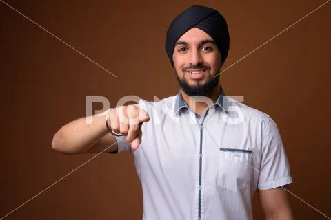 Young bearded Indian Sikh man wearing turban against brown backg Stock Photos