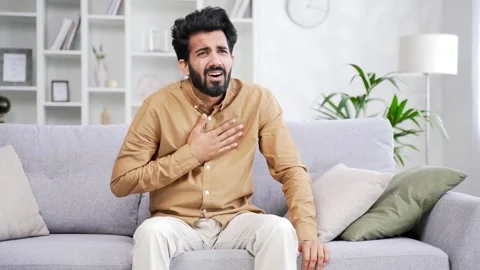 Young bearded male having a panic attack while sitting on sofa in living room  Stock Footage 252216170