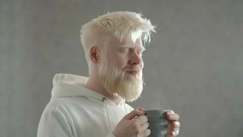 Young bearded man with albinism taking break to drink hot tea. White background Stock Footage 244844986