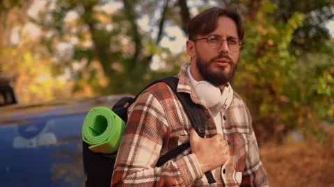 Young bearded man with backpack over shoulder, looking at camera, describing the Stock Footage 278277292