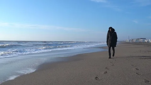 Young bearded man in black clothes is walking along the beach at the sunny day. Stock Footage 127255166
