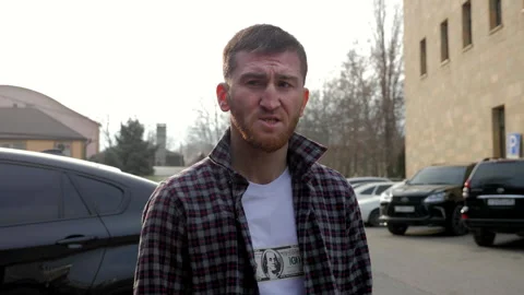 Young bearded man with broken nose adjusts shirt on street Stock Footage 285408889