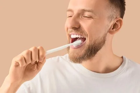 Young bearded man brushing teeth on beige background, closeup Stock Photos