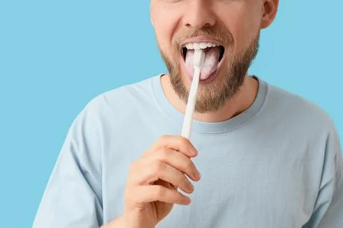 Young bearded man brushing teeth on blue background, closeup Stock Photos