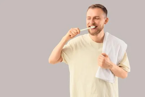 Young bearded man brushing teeth on light background Stock Photos